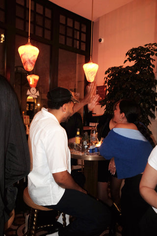 One man and two women sitting at a table in a bar. The man and one of the women are giving each other a high five. The room is dimly lit and the atmosphere is cheerful and comfortable. 